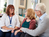 An older woman and man, sitting on a sofa, talking with a support worker.