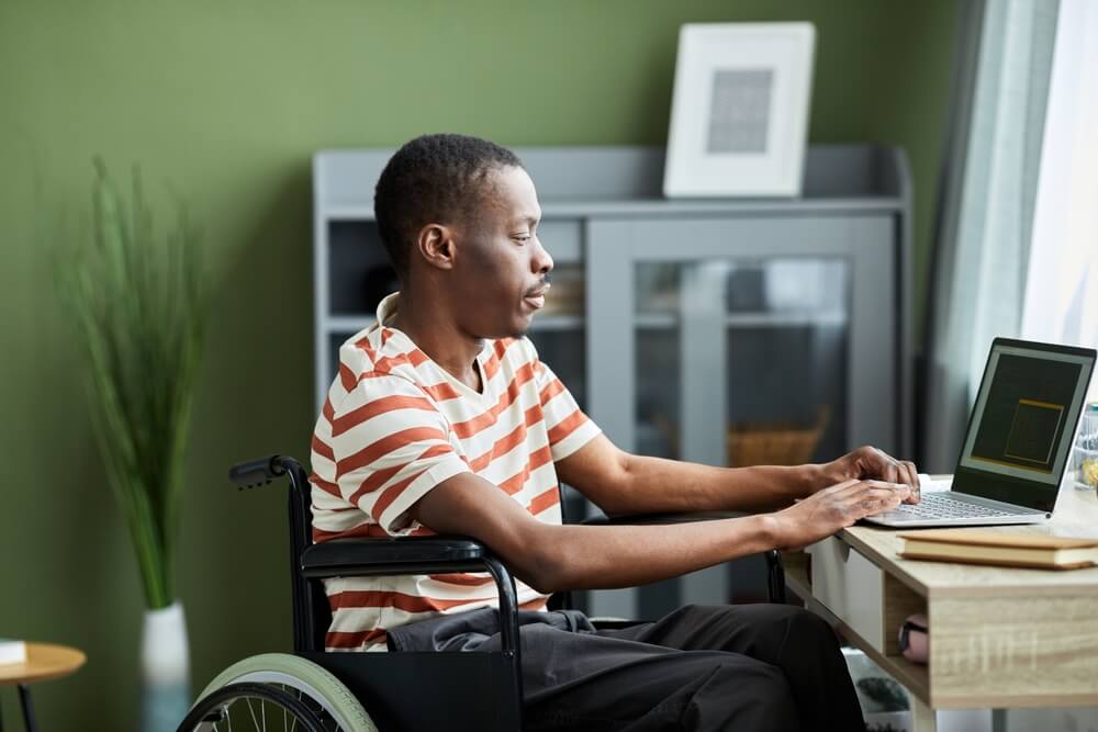 Photo of a man, in a wheelchair, sat at a laptop.