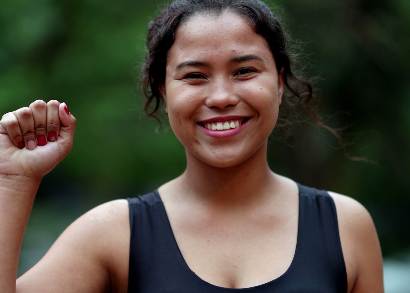 Photo of a young woman smiling, holding up her right hand in a fist.