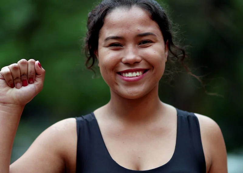 Photo of a young woman smiling, holding up her right hand in a fist.