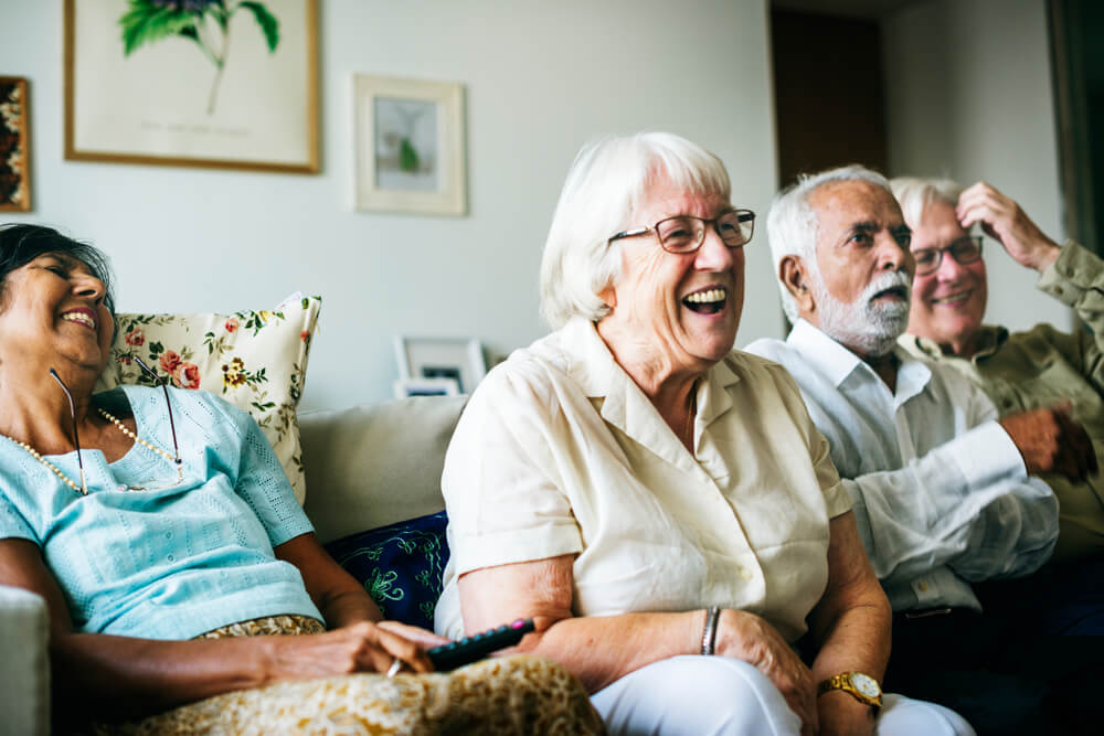 Group of older people sat together on a sofa, leaning forward and laughing.