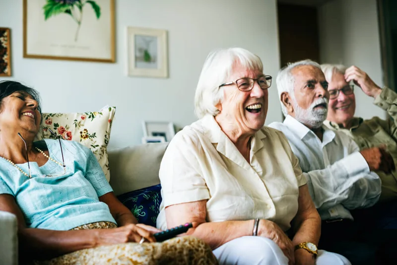 Group of older people sat together on a sofa, leaning forward and laughing.