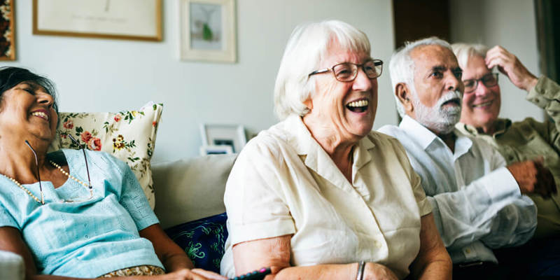 Group of older people sat together on a sofa, leaning forward and laughing.