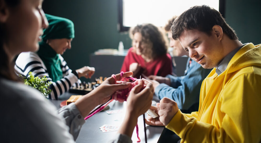 Photo of a group of people with learning disabilities doing arts and crafts projects, focused in on a young man, smiling. 