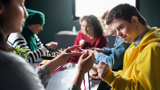 Photo of a group of people with learning disabilities doing arts and crafts projects, focused in on a young man, smiling. 