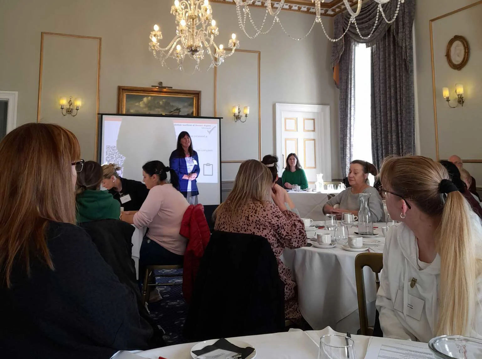 Woman stood at front of room full of people leading a presentation