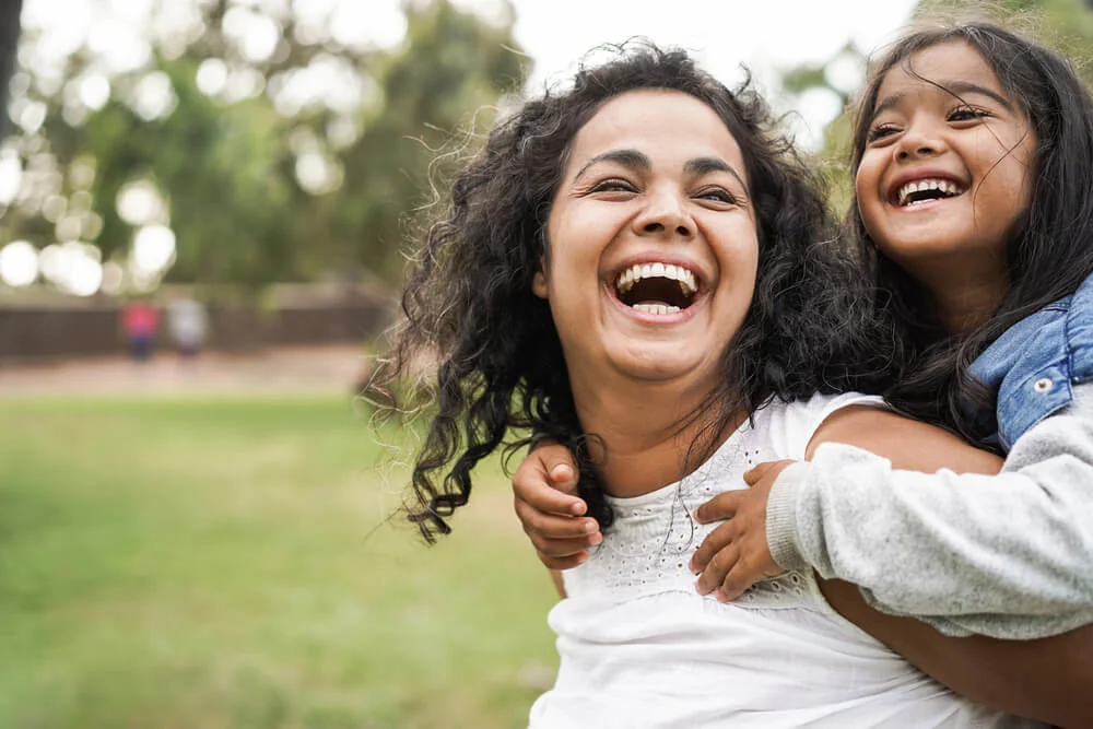 A woman giving a piggyback to a child, both smiling.