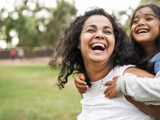 A woman giving a piggyback to a child, both smiling.