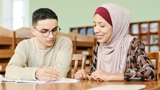 Two young adults sat at a table looking over papers.