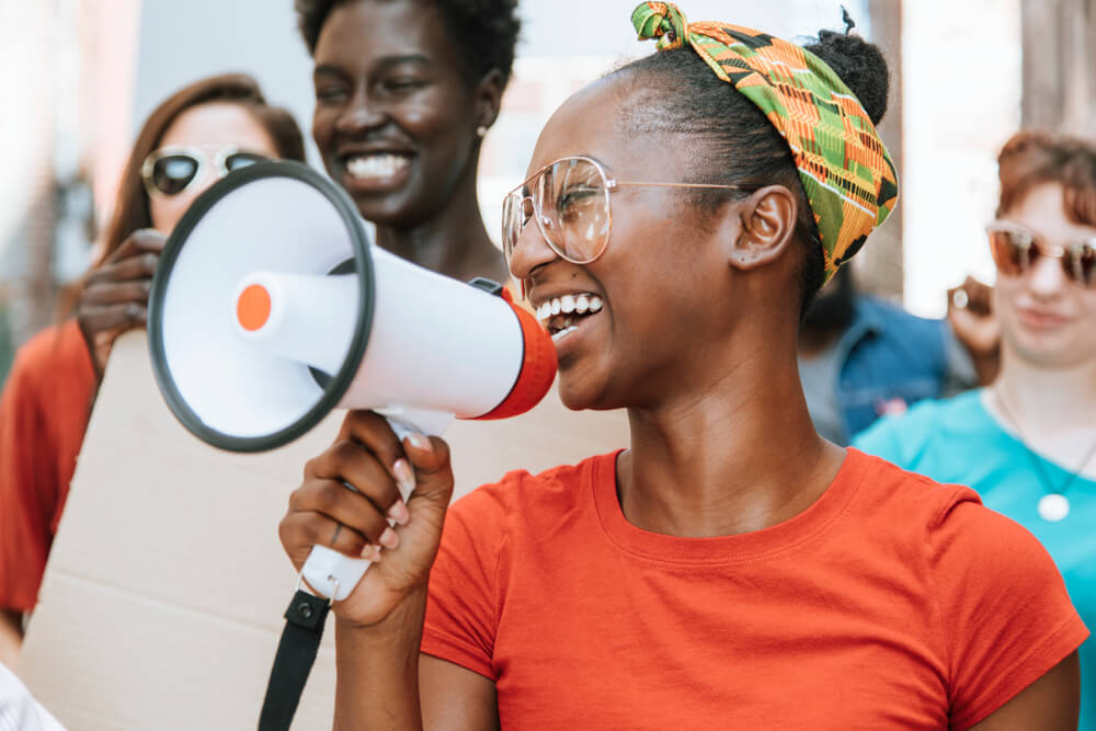 Photo focused on a young woman, smiling, with a megaphone.