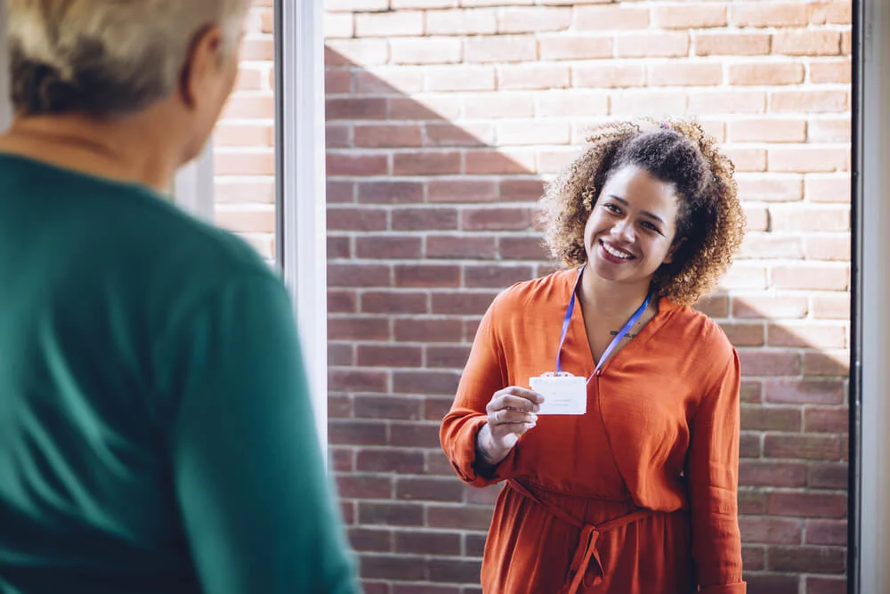 Photo of a social worker at a woman's front door, showing her identity badge, smiling